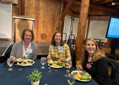 Oregon Geriatrics Society 2025 Conference - three attendees sitting at a table eating dinner - blue tablecloth, lovely centerpiece, podium in background, rustic lodge